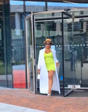 Woman in a bright green dress and white coat exiting a building.