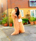 Woman in a long, light pink dress standing on a street with potted plants in the background.