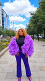 Person wearing a vibrant purple outfit with ruffled sleeves in an urban setting.
