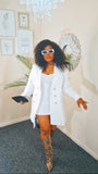 Woman in a white coat and sunglasses standing in a room with decor elements.