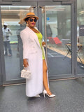 Woman in a structured white statement coat and green top standing in front of glass doors.