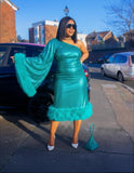 Woman in a teal dress with ruffled sleeves standing on a street.